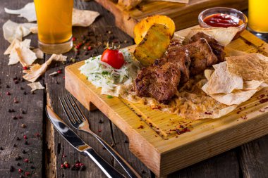 Pita ekmeğine domuz şiş. Yakınlarda pita ekmek cipsi ve kızarmış patates dilimleri var. Yanında Gürcü soslu şeffaf cam bir sos kasesi var. Salamura soğan ve domates yan yana yatar. Yiyecek tahtanın üzerinde yatıyor. Tahta dar bir çizgide duruyor.