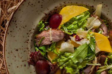 Salad with meat, basil, young shoots, grapes, lemon and salad in a plate on a straw background