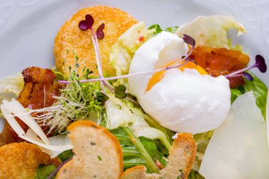 Salad with bacon, fried egg, sprouts, fried bread, salad, cheese in a plate on a light table