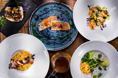 On a wooden table there is a sauce in a jar, a plate with shrimps, sprouted sprouts, avocado and purple mung bean salad, in the second plate a slice of puff pancake cake, salmon caviar, Philadelphia cheese, sauce and salad sprouts, in the third plate