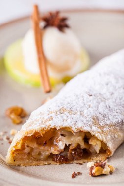 Elma, kuru üzüm, tarçın, pudra şekeri ve cevizli çörek, ince bir hamur kabuğunda pişirilmiş. Turta seramik bir tabakta, yanında bir top vanilyalı dondurma ve bir nane yaprağı var. Ahşap arkaplan