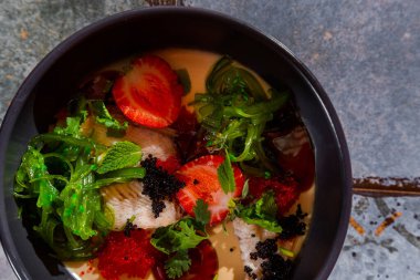Salad with eel, strawberries, chuka, two-color tobiko caviar, parsley and sauce in a plate on the table
