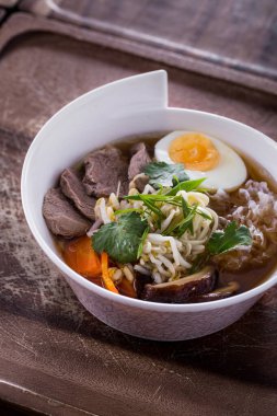 Beyaz bir tabakta et, erişte, haşlanmış yumurta, maydanoz, mantar, havuç, taze filizler ve soğanlı çorba.