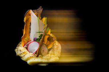 On a black background, there are mashed potatoes with radishes, flower petals, fruit, lace chips, mung bean salad, green pea sprouts, and dry mango. Long exposure blurred photo