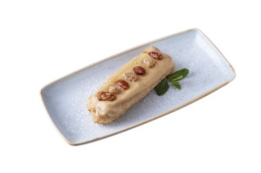 Eclair with condensed milk, walnuts, almonds and mint in a plate on a white background
