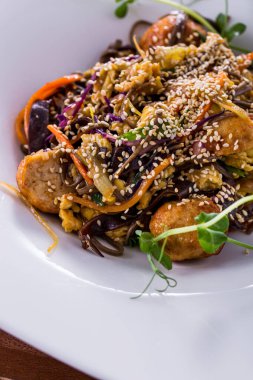 Salad with meat, sesame seeds, pea sprouts, spaghetti, and mung bean salad in a plate on a wooden background