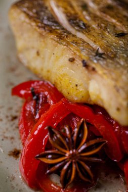 Fried fillet of sebasa, with chopped pickled peppers and baland on a creamy round plate, close-up. Vertical orientation 