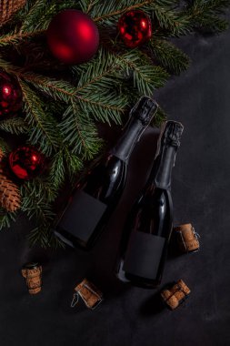 Köknar dalları ve Noel süslemeleri ile siyah bir masanın üzerinde duran mantarlı şampanya şişeleri.