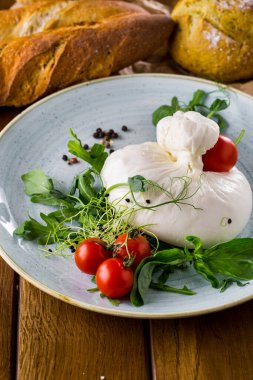 Salad with tomatoes, mozzarella, basil, arugula, pea sprouts, peppercorns in a plate on a wooden table with bread