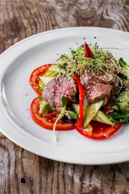 Salad with meat, tomatoes, mung bean salad, young shoots, lettuce, cucumbers and peppers in a plate on a wooden background