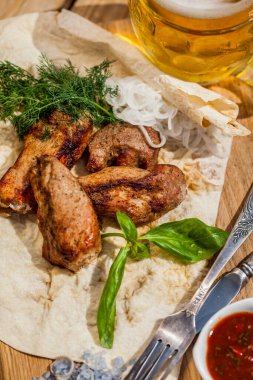 Maydanozlu domuz şiş ve fesleğenli pide ekmeği. Yakınlarda bir çatal ve bıçak var, soğan halkaları turşusu. Tencerede erik sosu. Ahşap bir tahtanın üzerinde yemek ve sos duruyor. Tahta tahta bir arka planda duruyor. Büyük bir bardak bira ve çatal.