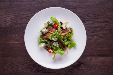 Salad with meat, lettuce, endive, pear, dor blue cheese, arugula in a plate on a wooden background