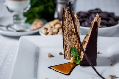 Waffle katmanlı bir dilim pasta çikolata jöleli, naneli, karamelli fındıklı, beyaz tabakta çikolata parçacıklı bir fincan kahve ve krema. Yatay yönelim