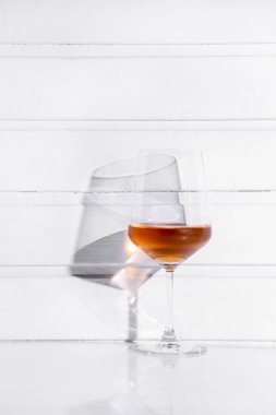 Rose wine in a glass standing on a white table and white wooden background