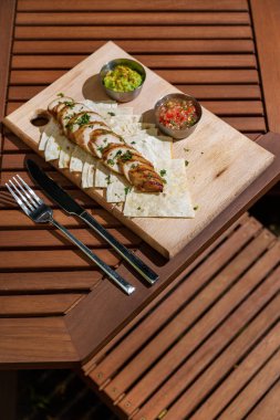 Pieces of meat with parsley, pita bread and two types of sauce in sauce bowls on a wooden board that lies on the table with cutlery