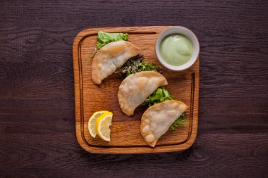 Yeşil salatalı küçük börekler, roka, limon dilimleri ve tahta tahtada beyaz sos. Yatay yönelim 