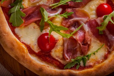 Pizza with cherry tomatoes, prosciutto, arugula and cheese on a wooden board