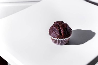 Chocolate cupcake in paper wrapper on white chair against white wooden wall background