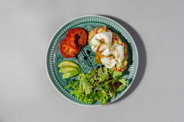 Avokado ve nar püresi ile karabuğday ekmekli bruschetta, üzeri kırmızı biberli haşlanmış iki yumurta. Yakınlarda roka soslu salata, üç dilim avokado ve iki dilim ızgara domates serpiştirilmiş. Yemekler yalan.