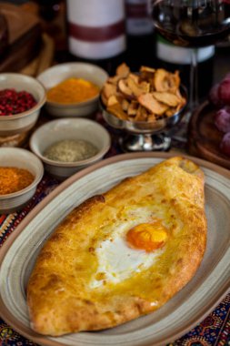 Tabağında yumurta, üzüm, kurutulmuş elma, baharat ve bir bardak kırmızı şarap olan Khachapuri. Dikey yönelim 