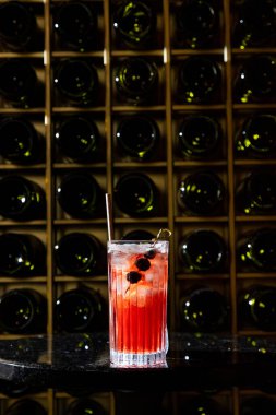 Cold, summer drink lemonade with raspberry syrup. Lemonade, raspberry syrup and ice cubes are poured into a tall, glassy, transparent glass. In a glass, a skewer with blueberries. The glass stands on a black stone round table. Behind the table is a w