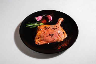 Raw chicken half chicken with bone, peppercorns, paprika, rosemary and garlic in a plate on a white background