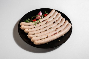 Raw sausages with peppercorns, thyme, rosemary and garlic in a plate on a white background