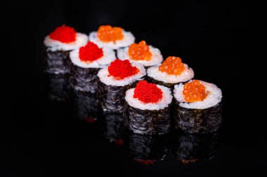 Roll with salmon, caviar, tobiko caviar, cucumber, rice, nori on a black mirror background