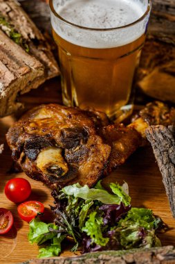 Bir bardak birayla domuz budu, kiraz domatesleri, ahşap bir tahtada ahşap marul ve akasya kütükleri.