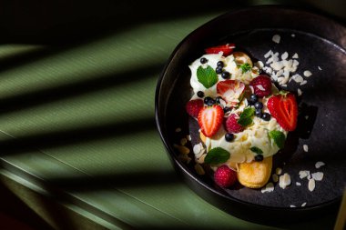 Cake with almond slices, strawberries, raspberries, mint and sauce in a plate on the table