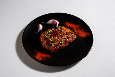Fried pork steak with peppercorns, paprika, salt, thyme and garlic in a plate on a white background
