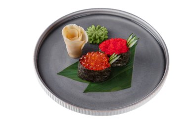Roll with red salmon caviar, flying fish caviar, cucumber, nori on a banana leaf with wasabi, ginger on a platter on a white plate