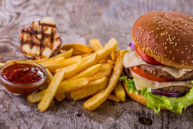 Burger with sesame bun, double cutlet, tomatoes, onions, lettuce, double cheese and mayonnaise with fries, garlic and sauce on a wooden table. Horizontal orientation