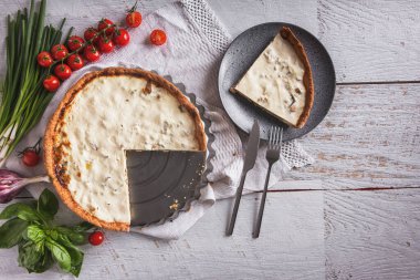 Cheese casserole with tomatoes, basil, garlic, onion and parsley on a towel with cherry sprigs and a piece of casserole on a plate on the table