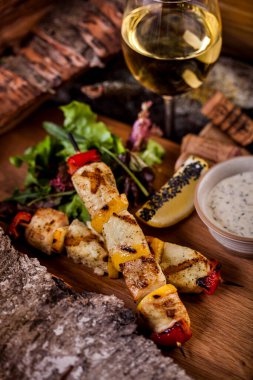 Fish fillet on a skewer, kebab lula with white sauce and parsley, a slice of lemon and sesame seeds on a wooden plate with a glass of belovin. Vertical orientation 
