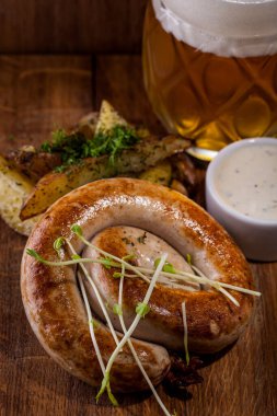 Izgara sosis, patates dilimleri ve ahşap arka planda doğranmış dereotu bir bardak bira ve sarımsak sosuyla birlikte beyaz bir tencerede..