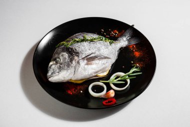 Raw dorado with peas, onions, paprika, chili, salt, thyme, rosemary and garlic in a plate on a white background