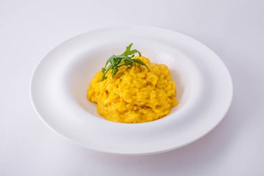 Risotto with four types of cheese and arugula leaves in a white, deep plate on a white plate.