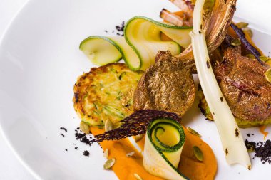 Altın yapraklı pirzola, sos, kabak, tohum ve beyaz tabakta dantel cips. Yatay yönelim