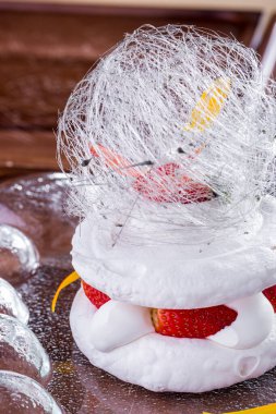 Dessert with frozen meringue, cream, sugar string, strawberries, flower petals on a sugar background. Vertical orientation