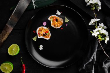 Rice snacks with salmon, lime, sweet potatoes, chili and parsley in a plate on a black table with cherry branches and a dark cloth