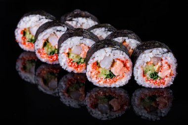 Roll with scallops, shrimps, rice, nori, cucumber, tobiko caviar, Philadelphia cheese, and onions on a black mirror background