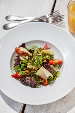 Peynirli salata, domates, biber, hindiba, marul ve ceviz bir tabakta bir çatal ve bir bardak meyve suyu ile birlikte.