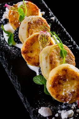 Ekşi kremalı, naneli, mikro yeşil, böğürtlenli, ahududulu ve yenilebilir yapraklı peynirli kekler. Siyah bir levhada yatıyorlar. Siyah bir arkaplanda.