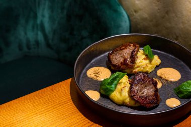 Grilled pieces of meat with mashed potatoes, basil and sauce in a plate on the table