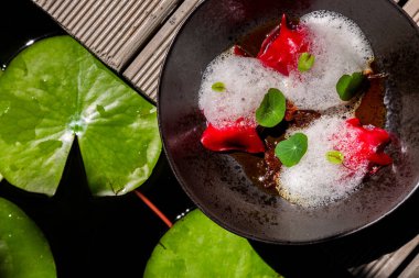 Red candy with apples, edible leaves, jam and froth on a plate and gray background