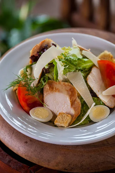 Salad with ham, endive, dill tomatoes, croutons, lettuce, cheese, in a plate on a wooden background