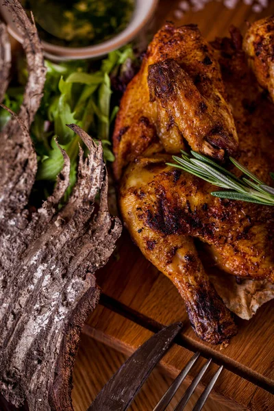 Sarımsak soslu ızgara tütün tavuğu. Yakınlarda bir çatal ve bir bıçak, sarımsak soslu ve satsibeli soslu bir sos kabı var. Tavuk bir tabak pide ekmeğinin üzerinde yatıyor. Lavaş ve çatal bıçak seti ahşap bir tahtanın üzerinde, yanında bir bardak r var.