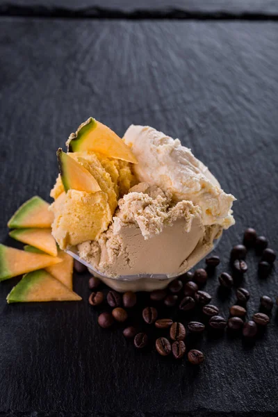 Vanilla ice cream scoops with melon pieces and chipped coffee beans on a stone background. Vertical orientation
