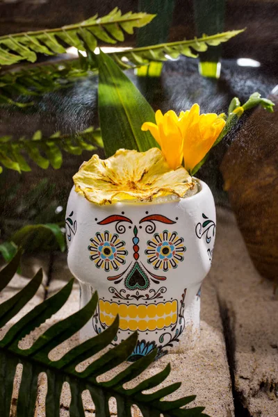 Buzlu kokteyl, kurumuş ananas ve beyaz bardakta duran bir çiçek.